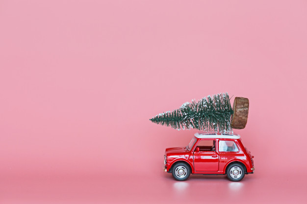 rode-speelgoedauto-met-een-kerstboom-op-het-dak-op-roze_107592-779